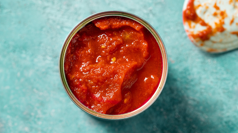 Open can of tomatoes on blue surface, overhead view