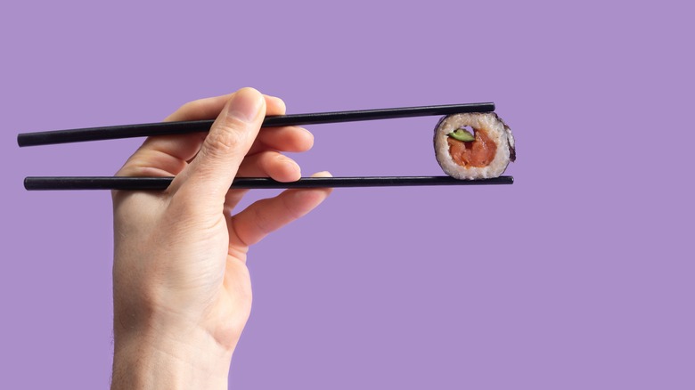 Hand holding chopsticks with sushi