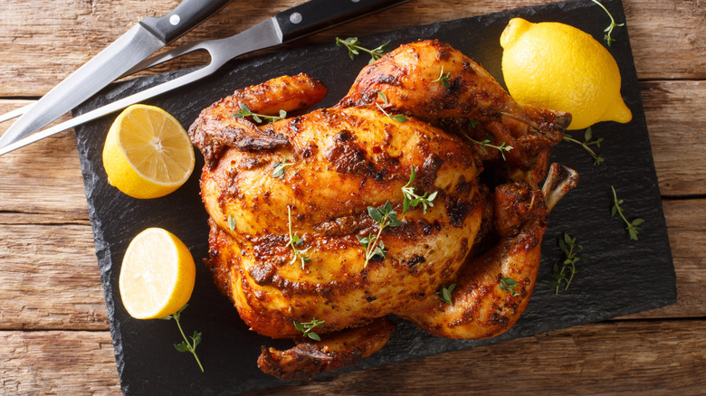 A seasoned rotisserie chicken on a cutting board with lemons and utensils