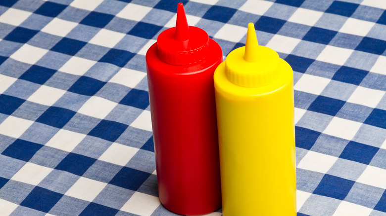 Ketchup and mustard bottles on blue and white plaid tablecloth.