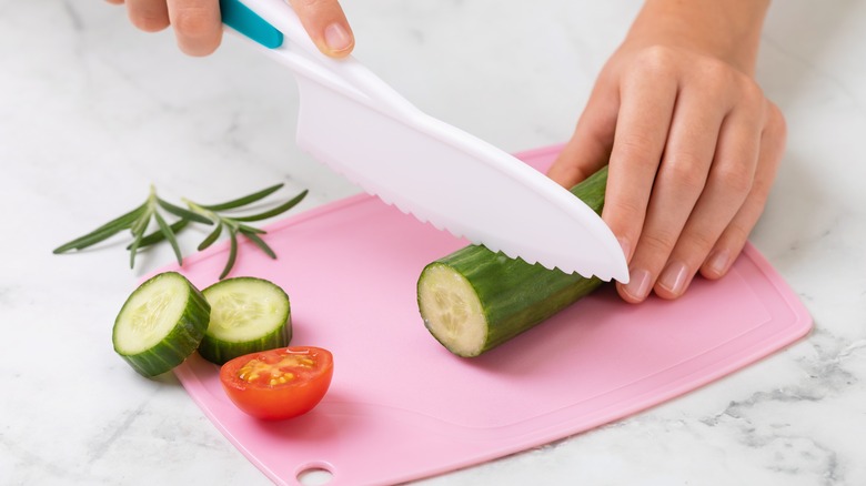 Hands slicing a cucumber on a plastic cutting board