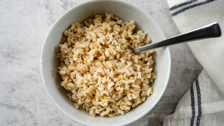 A bowl of cooked brown rice with a spoon and striped napkin