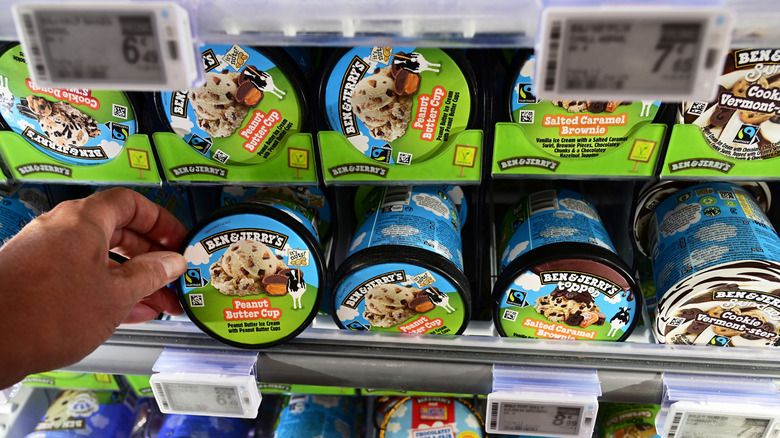 Hand selecting pint of Ben & Jerry's ice cream from freezer case.