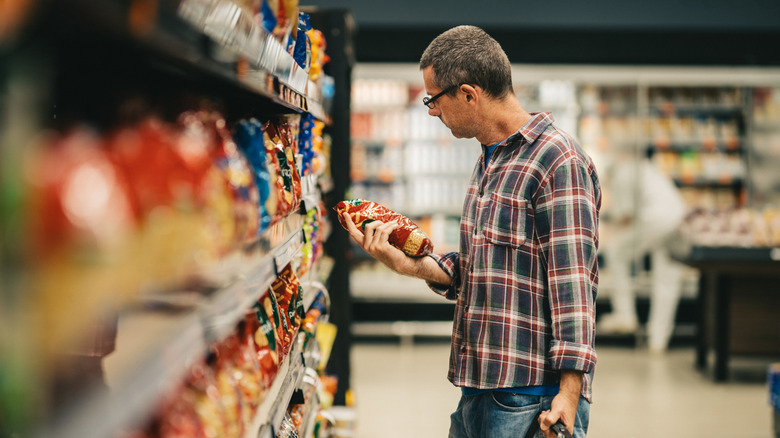 Man standing in snack aisle looking at package.