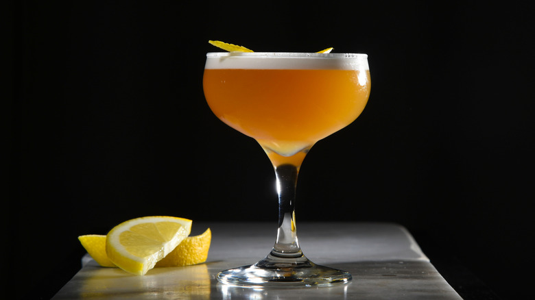 Amaretto sour in a glass with sliced lemons nearby