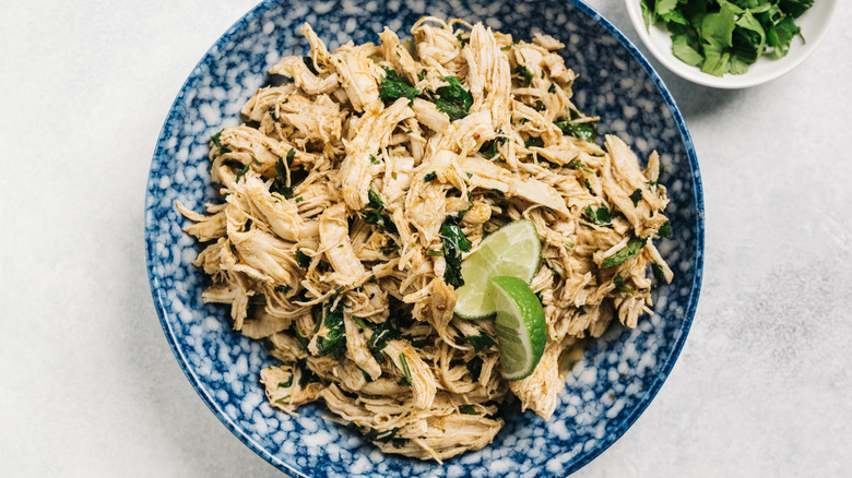 Shredded chicken in blue and white dish with lime wedges.