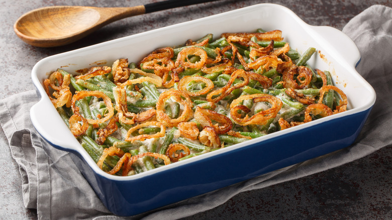 Green bean casserole with cheesy mushroom sauce and topped with crispy onions close-up in a baking dish on the table.