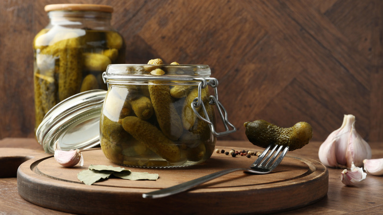 Pickles in jar, on a fork and spices on wooden table