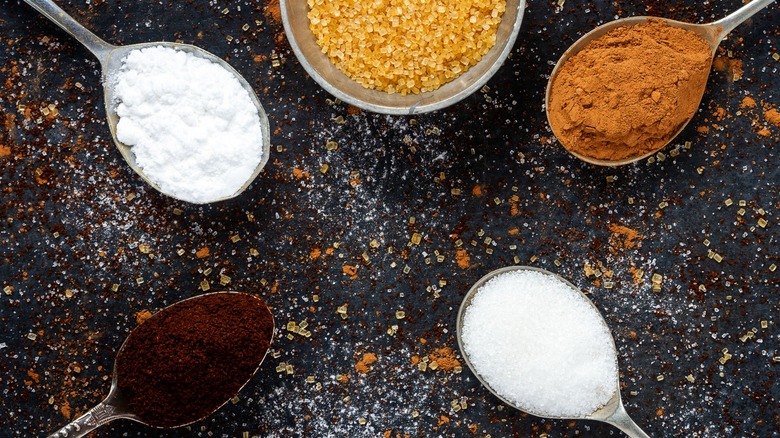 Powdered sugar, coffee, cinnamon, and table sugar in spoons on sugar dusted surface