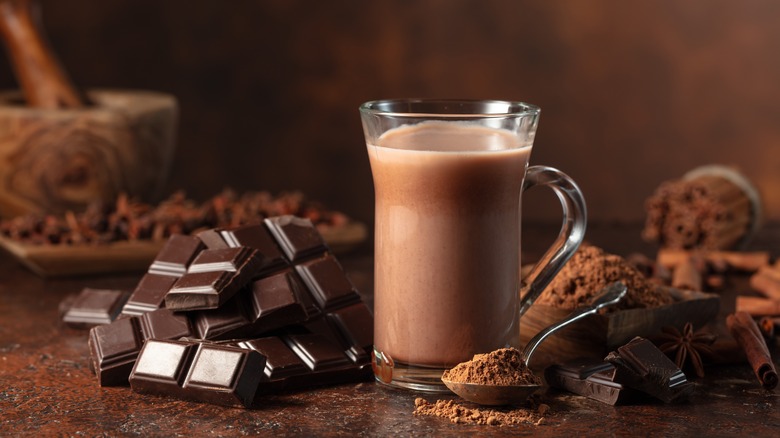 Glass of chocolate drink next to pieces of chocolate and spoon of cocoa powder