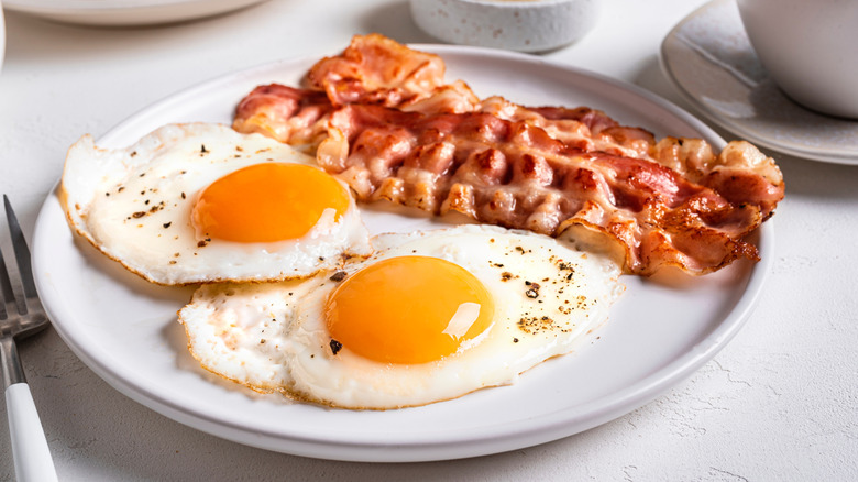 A close up image of fried eggs and bacon served on a plate.