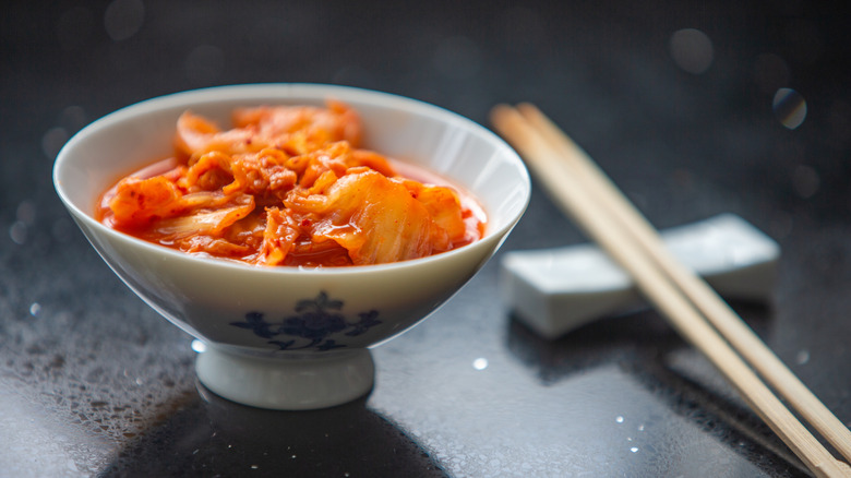 Small porcelain bowl with kimchi, alongside chopsticks and on black surface