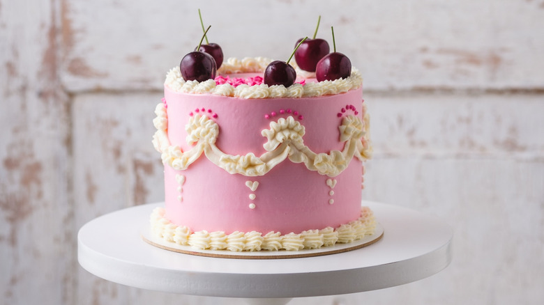 Pink Lambeth cake with white accents topped with fruit.