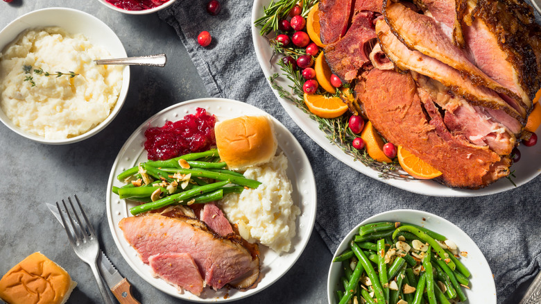 A ham is served for dinner alongside sides in bowls