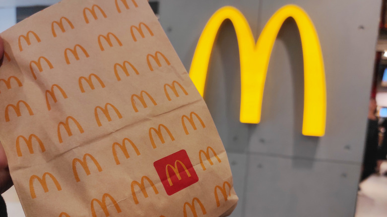 McDonald's branded paper bag held up against Golden Arches sign