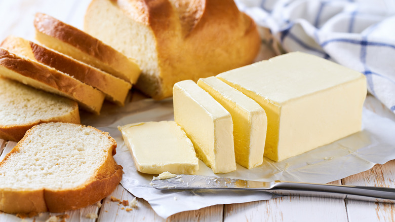 A block of butter sliced with a butter knife beside fresh bread.