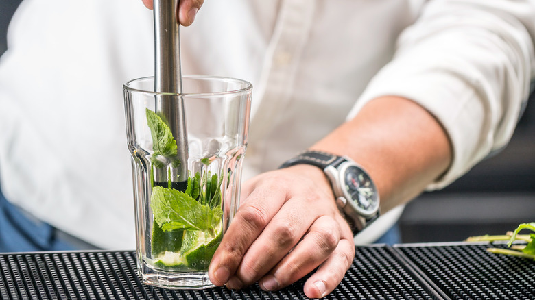 bartender muddling lime and mint in a glass
