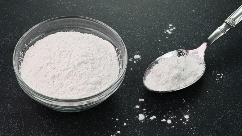 Dish of baking soda and spoon with baking soda on a gray-black background.