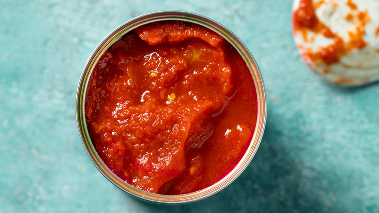 Top view of an open can of canned tomatoes on a light blue background.