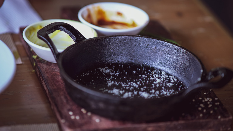 Cast iron skillet with salt on wooden cutting board with ramekins in background.