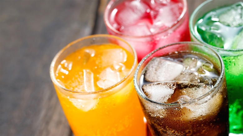 Four glasses with ice and different colored liquids inside