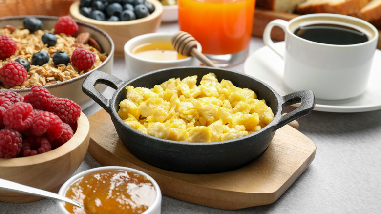 Breakfast spread, including coffee, jam, and fruit, with scrambled eggs at the center.