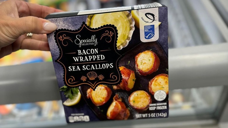 Hand holds up package of Aldi exclusive brand Specially Selected Bacon Wrapped Sea Scallops.