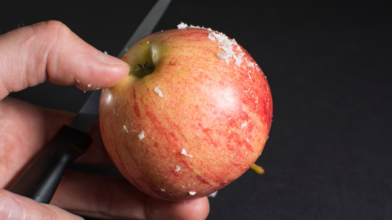 Hand holding an apple with knife, showing flakes of wax.