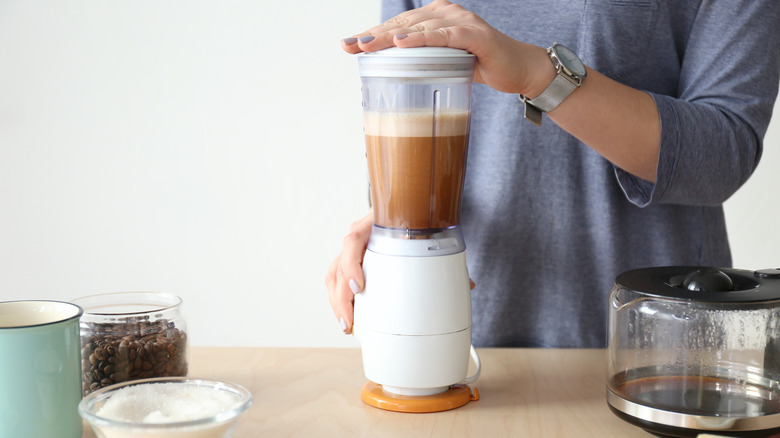 woman blending coffee with butter and oil in a small blender