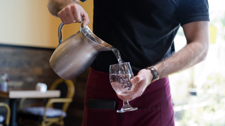 waiter pouring water from pitcher into wine glass
