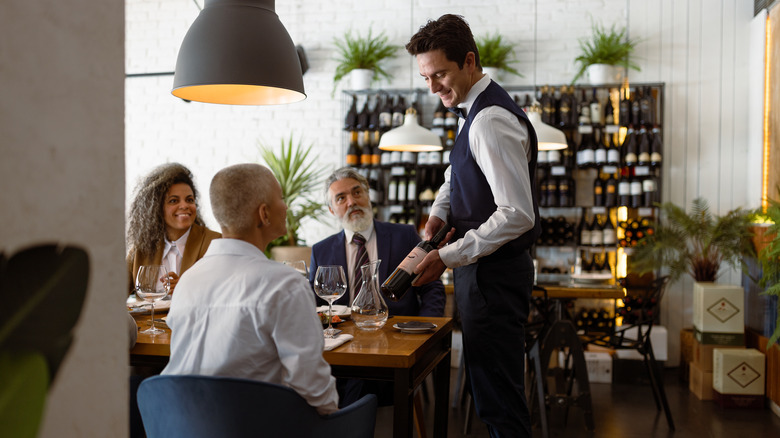 A sommelier serving wine to diners