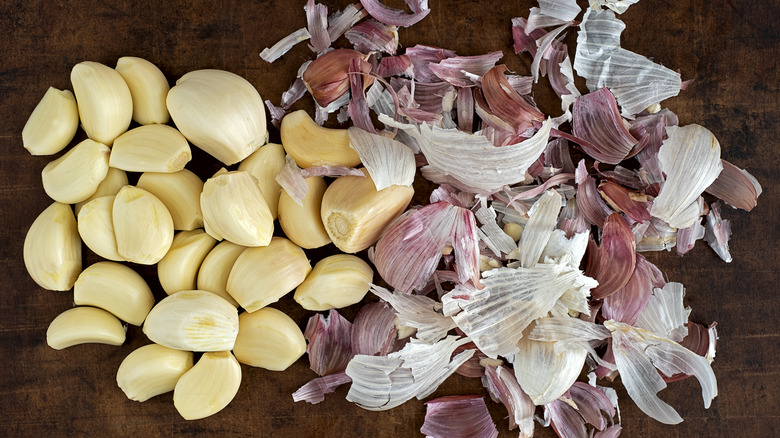 Peeled cloves of garlic next to a pile of papery skins. 