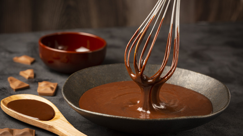 Dark bowl filled with melted chocolate, dripping off of whisk