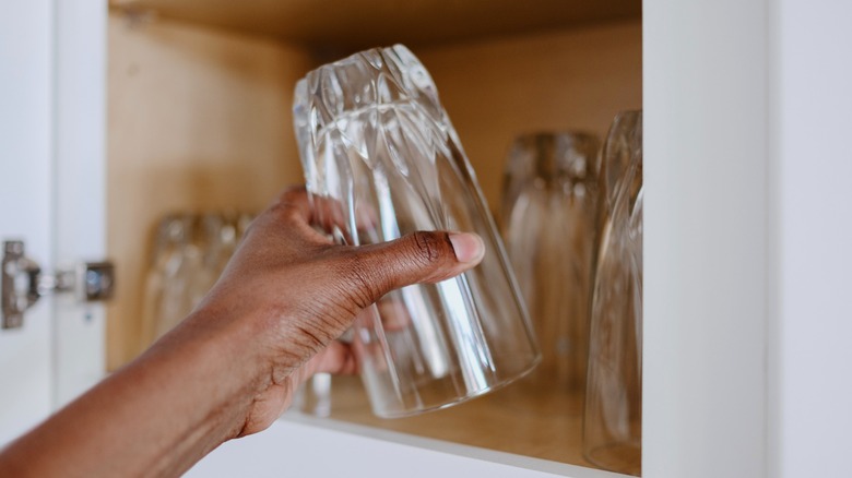 A person holding glass upside down in front of cupboard