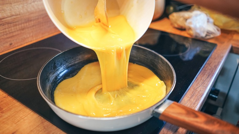 Beaten eggs being poured into frying pan on stove