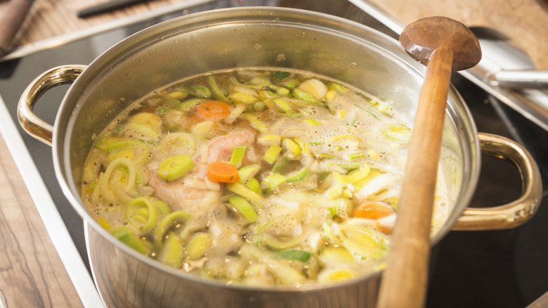 Large pot of vegetable soup with a wooden mixer on a stovetop with a wood countertop