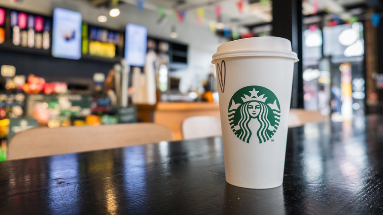 White and green Starbucks cup on table, store interior blurred background.