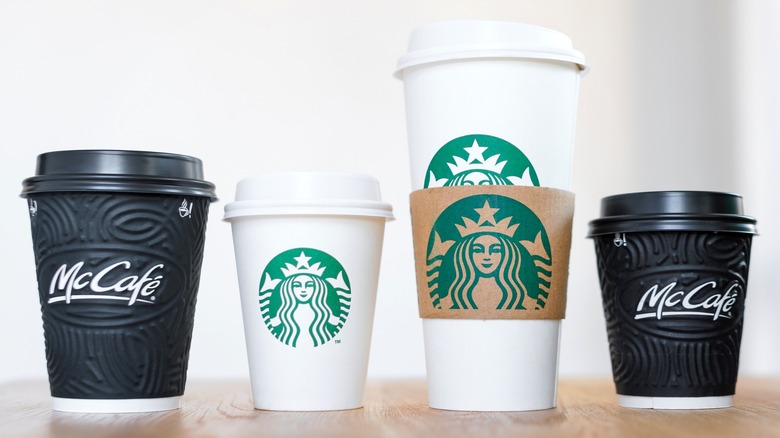 Two white Starbucks coffee cups between two black McCafé cups on wood table