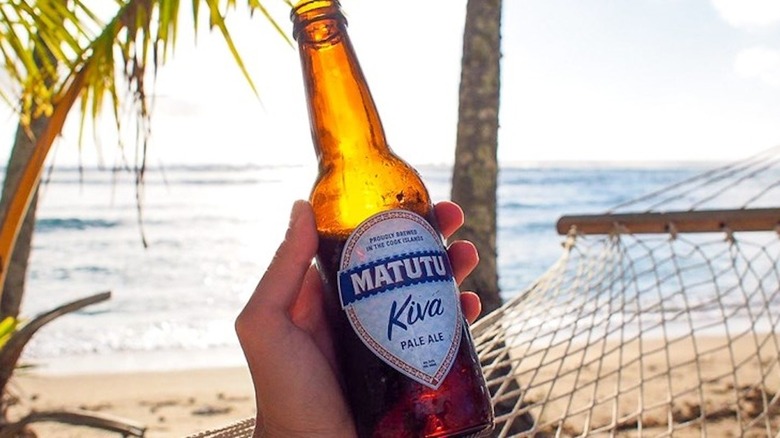 hand holding a bottle of Matutu pale ale against a beach background