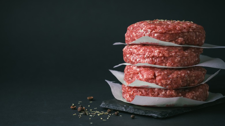 Four raw burger patties with paper