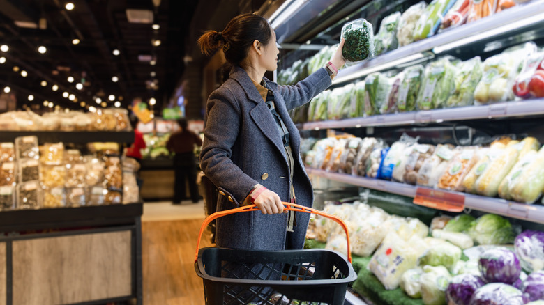 Woman picking up fresh produce from a refrigerated grocery store shelf