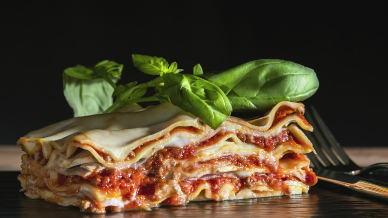 a close up of a portion of lasagne, topped with basil