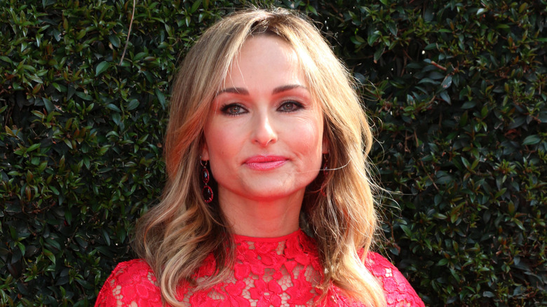 Giada De Laurentiis wearing a red lace dress, standing in front of a hedge