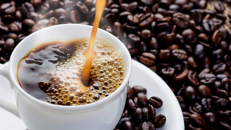 Coffee poured into white cup surrounded by coffee beans