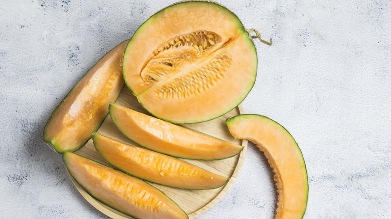 Overhead view of cantaloupe half and segments on cutting board.