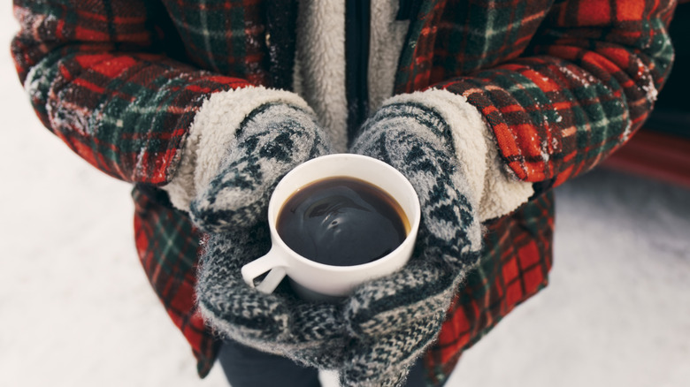 Person wearing cold weather clothing holding a white mug filled with coffee