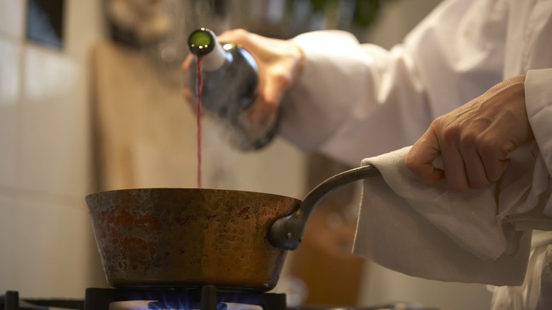 Chef pouring wine into pot on stove