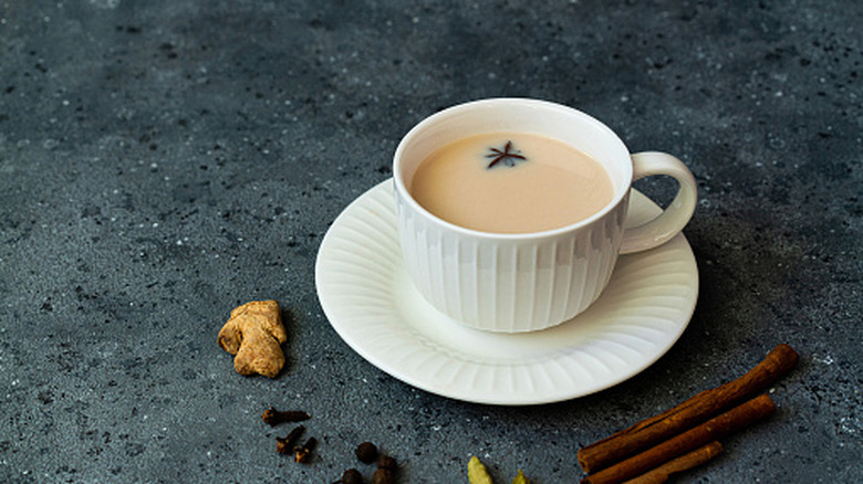 Chai with milk in cup and spices around saucer.