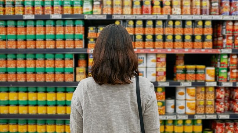 A woman with back to camera looks at a wall of canned vegetables.