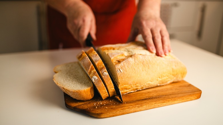 Person in red apron slicing a loaf of bread on wood cutting board..